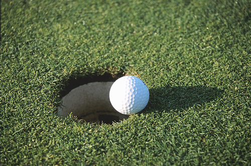 A golf ball is on the edge of the hole on a grass turf